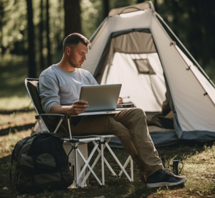 A man working outside on a laptop in front of a tent